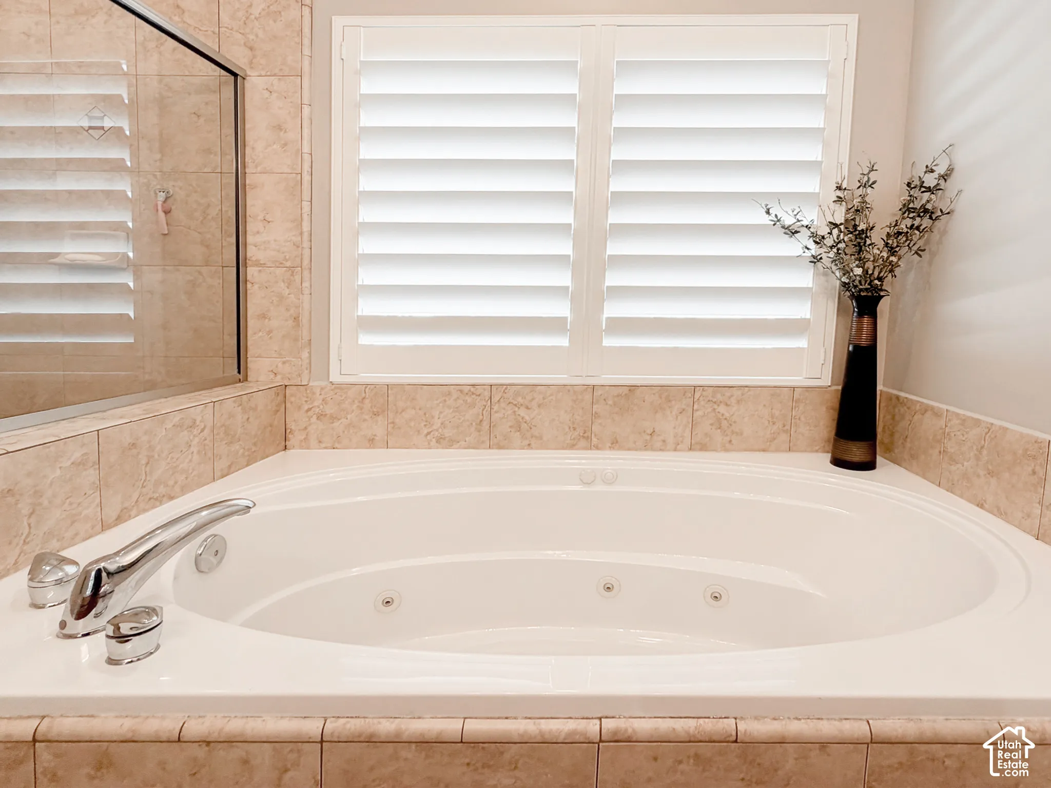 Soaking tub with integrated jets, chrome fixtures, tiled surround, and white louvered shutters