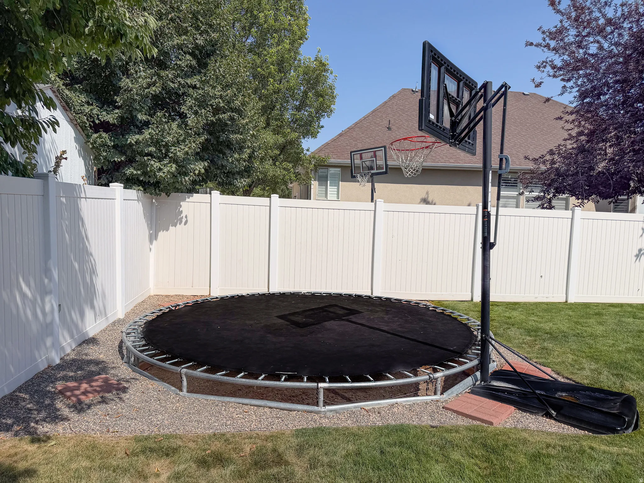 Expansive backyard featuring a white vinyl privacy fence, green lawn, and a gravel perimeter