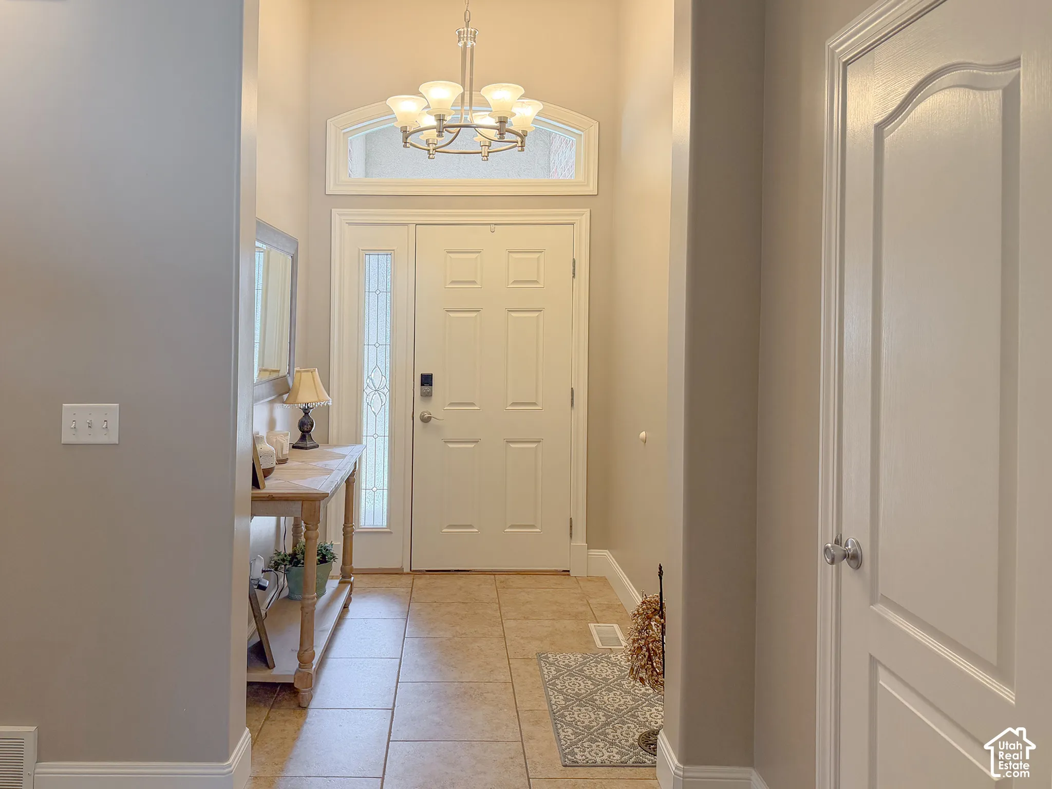 Entryway featuring a decorative chandelier, arched transom window, a tiled floor, and a paneled entry door with sidelight