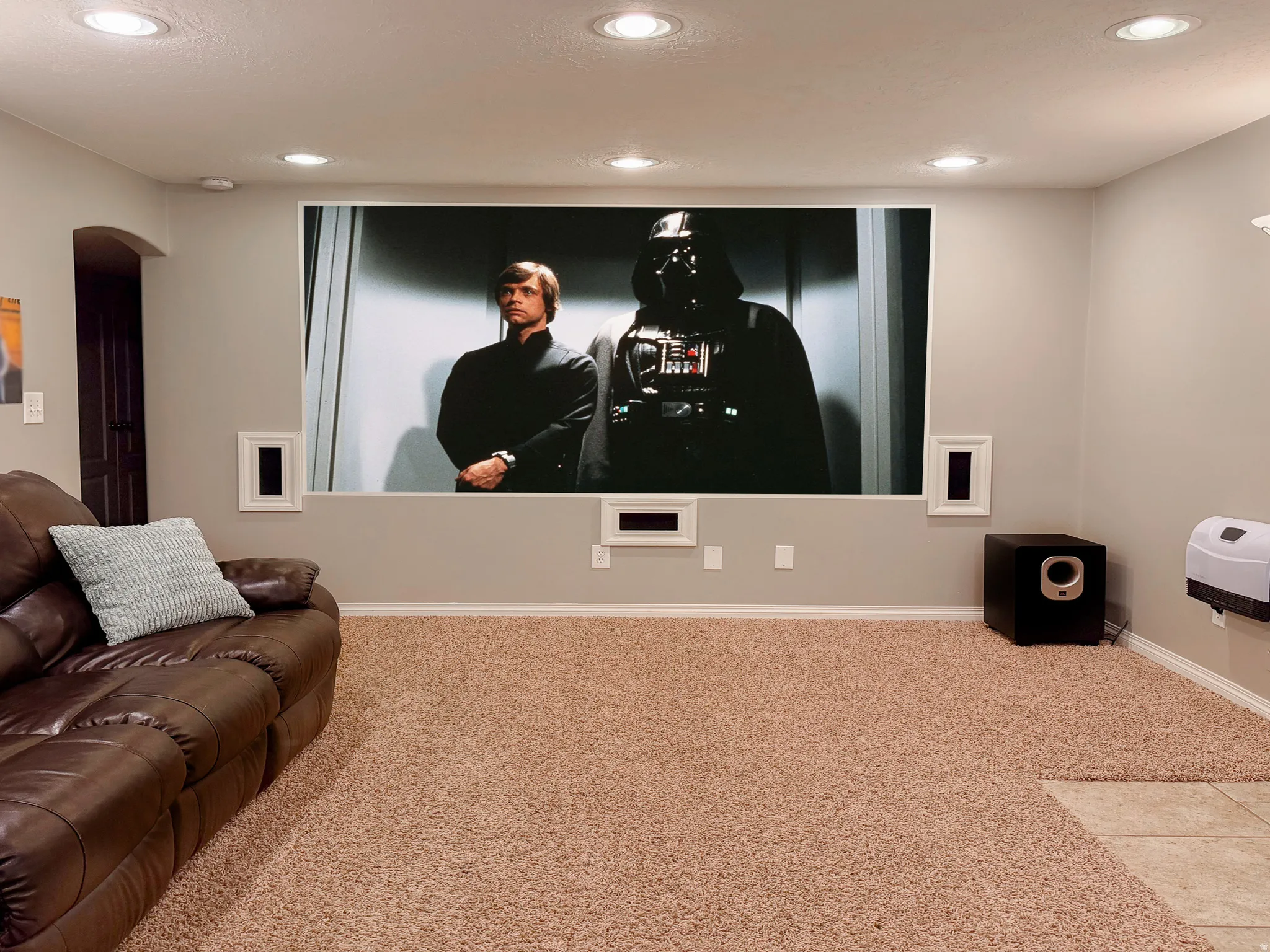 Media room featuring a large projection screen, recessed ceiling lighting, and wall-mounted speakers