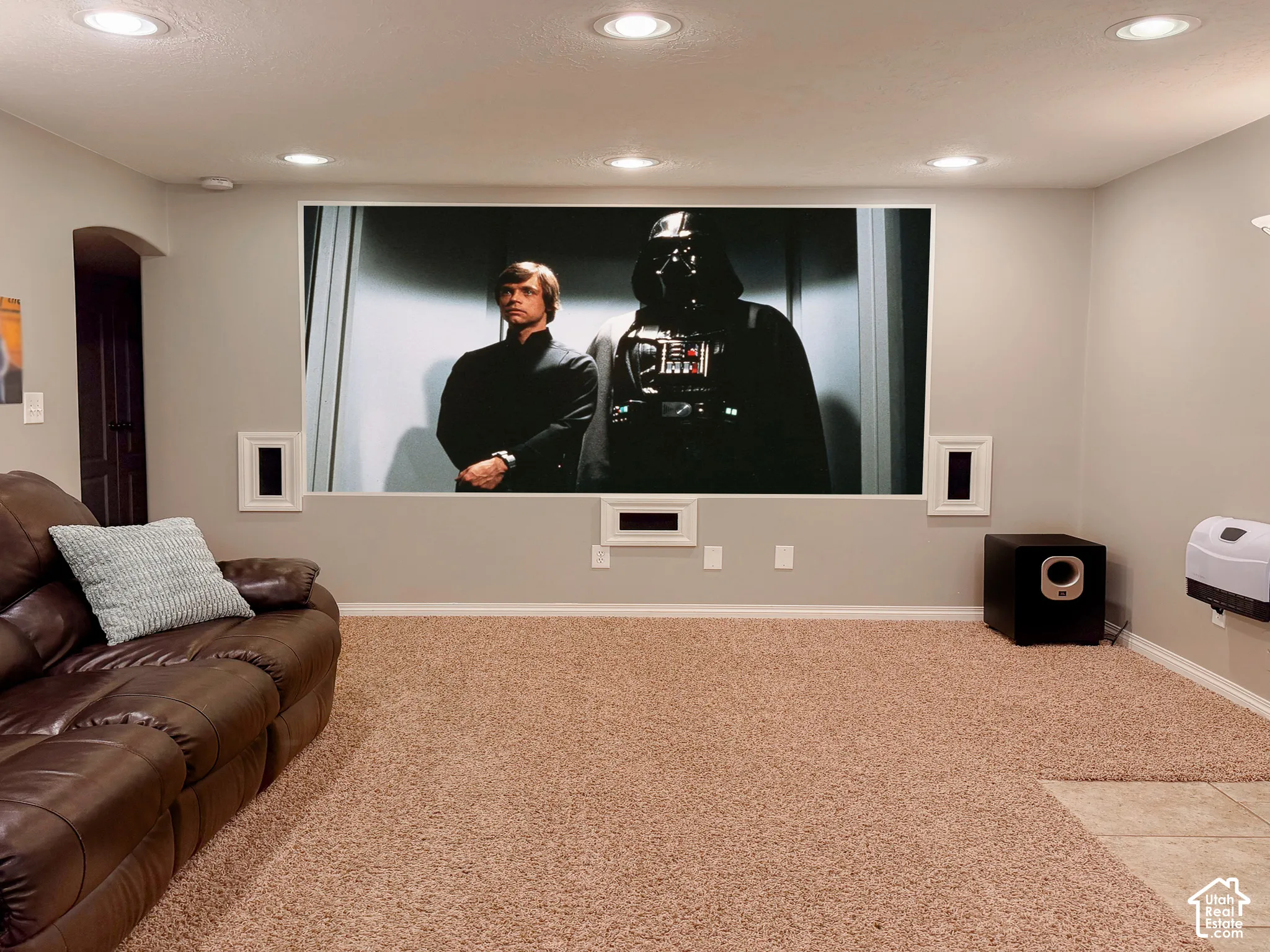 Media room featuring a large projection screen, recessed ceiling lighting, and wall-mounted speakers
