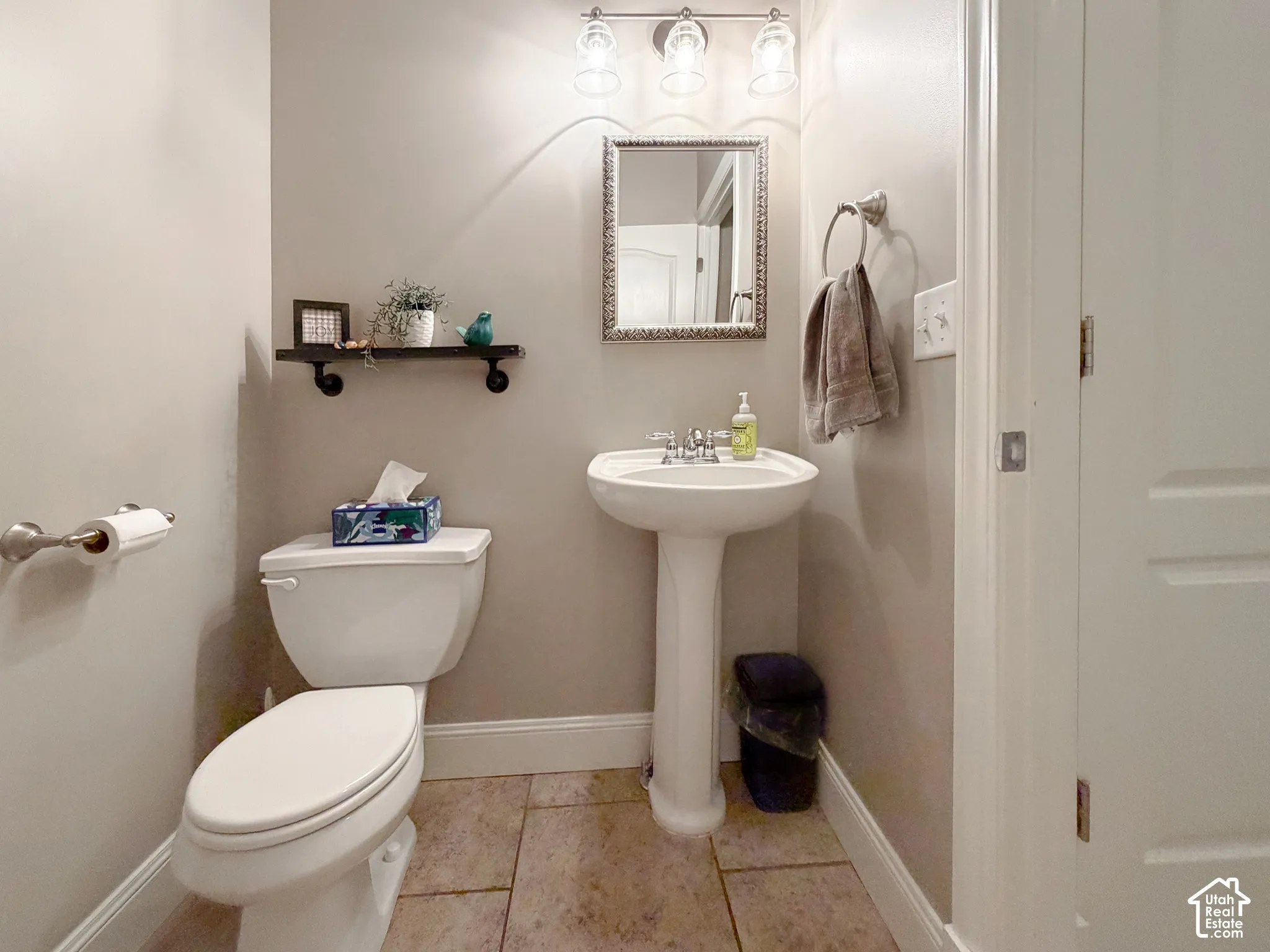 Pedestal sink with chrome faucet, wall-mounted light fixture, decorative mirror, and neutral wall paint