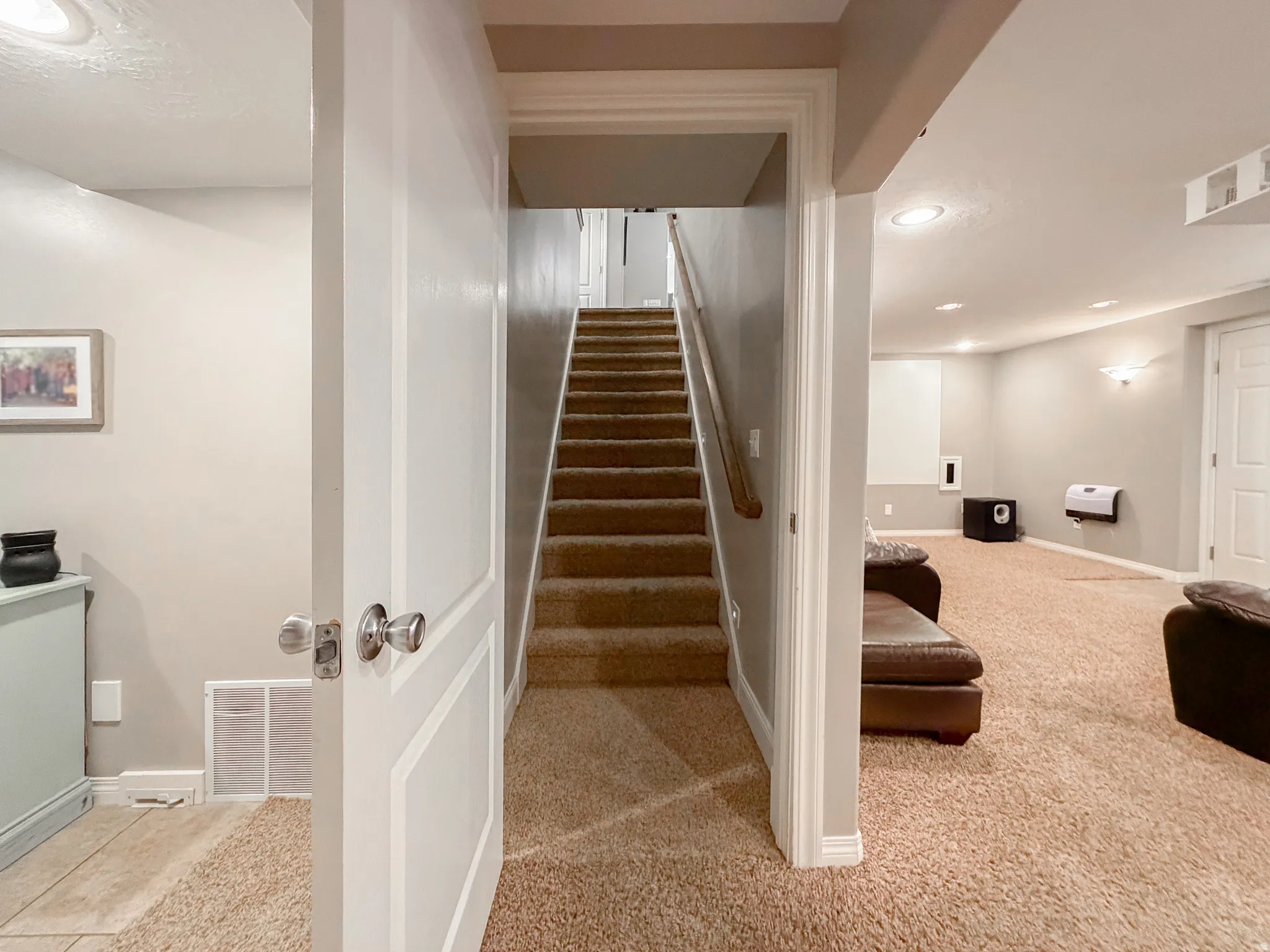 Carpeted stairs with wood handrail, recessed lighting, wall sconces, paneled door, and textured carpet flooring