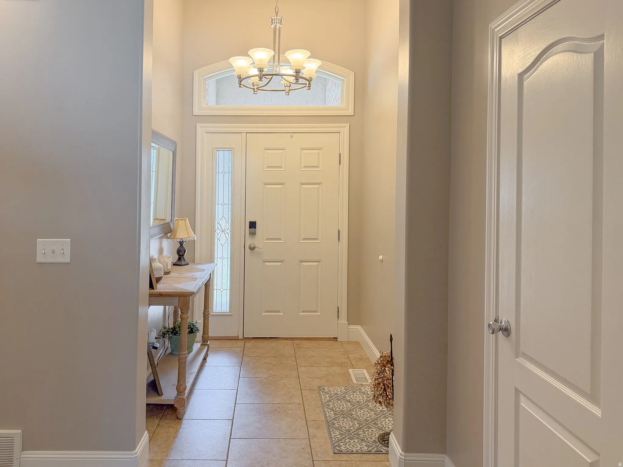 Entryway featuring a decorative chandelier, arched transom window, a tiled floor, and a paneled entry door with sidelight