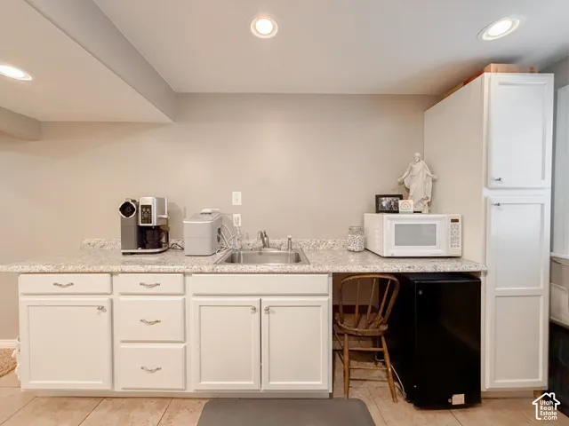 White cabinetry with silver-tone pulls, speckled countertop, stainless steel sink, recessed lighting, and tiled flooring