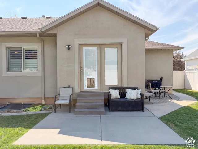 Exterior stucco finish, composite shingle roof, concrete patio, composite steps, and a glass-paneled exterior door