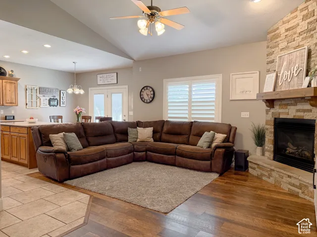 Vaulted ceiling with a ceiling fan, stone fireplace with a wood mantle, wood-finish flooring, white plantation shutters, and a recessed lighting