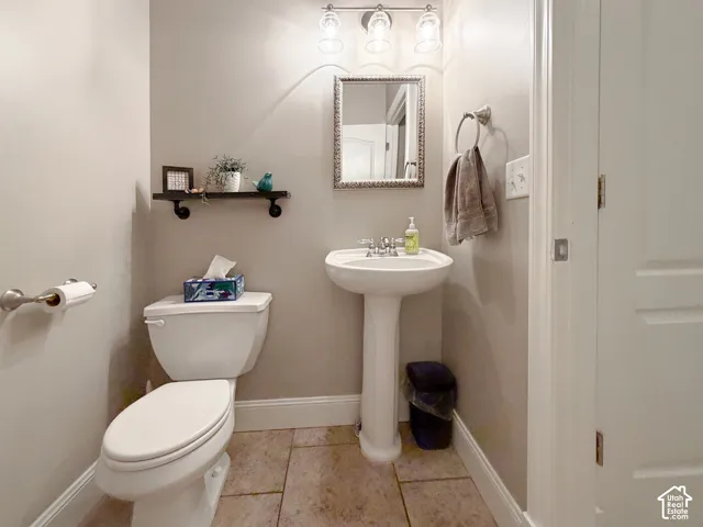 Pedestal sink with chrome faucet, wall-mounted light fixture, decorative mirror, and neutral wall paint
