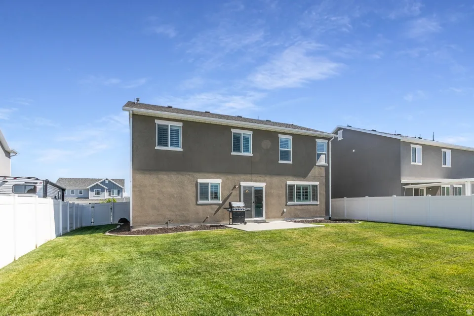 Expansive backyard featuring a lush lawn, white privacy fencing, a concrete patio, and a stucco exterior with multiple windows
