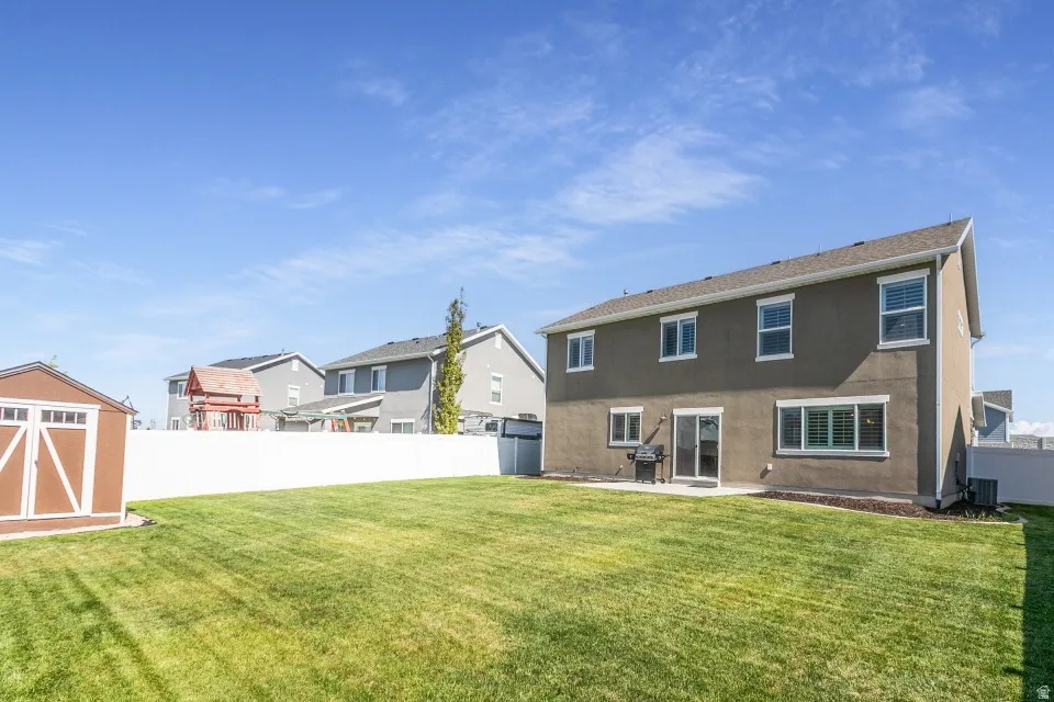Expansive grassy yard with a concrete patio, white privacy fencing, and a separate storage shed