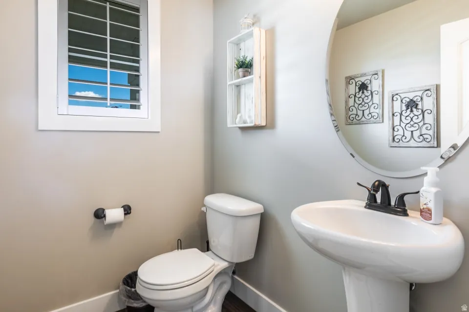 White plantation shutters, pedestal sink, wall-mounted mirror, and dark-finish faucet