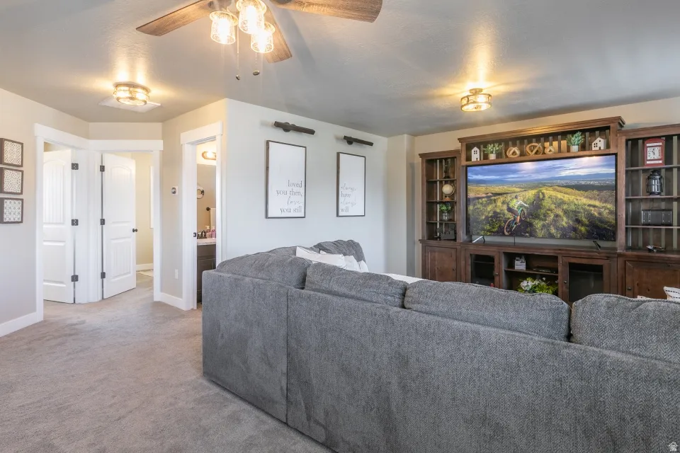 Built-in entertainment center with integrated shelving, wood-finish ceiling fan, recessed lighting, and soft carpeting