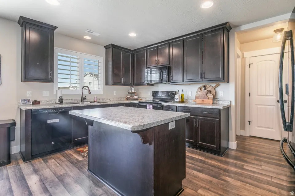 Spacious kitchen featuring dark wood-finish cabinetry, light-toned countertops, a central island, and wood-finish flooring