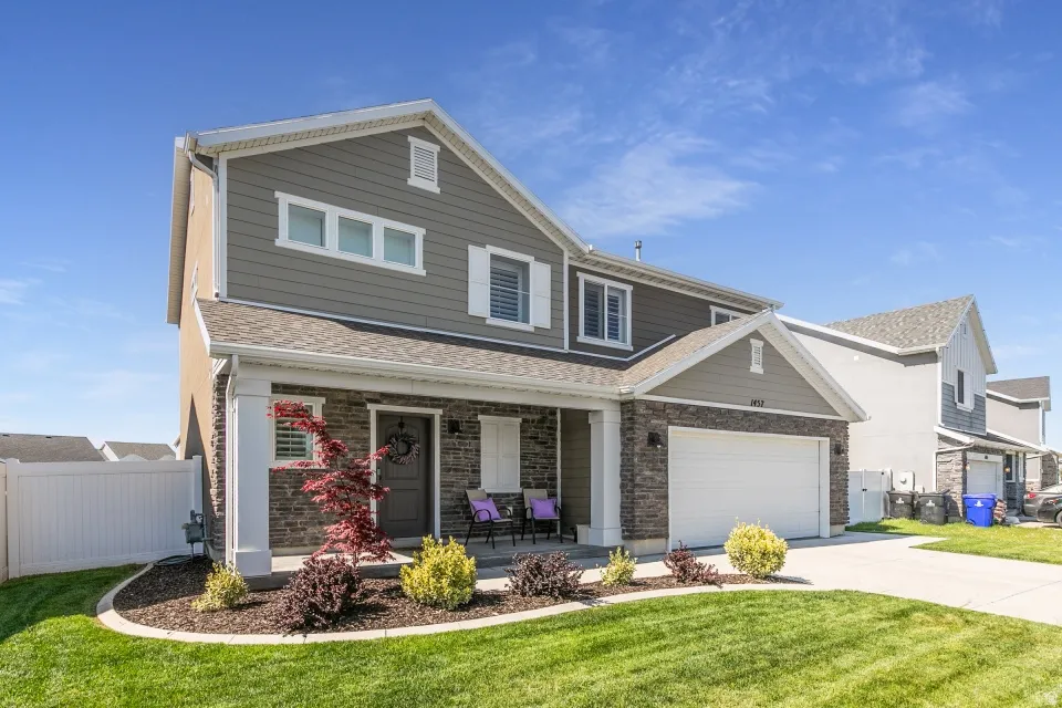 Two-story residence featuring a covered front porch, stone and siding exterior, an attached garage, and a concrete driveway