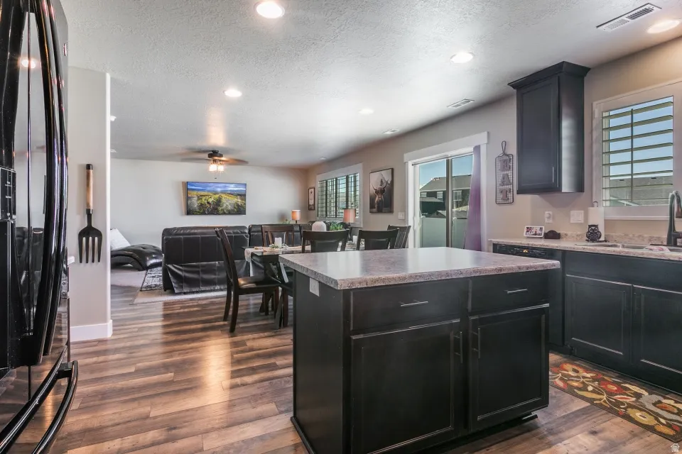 Open-concept living area featuring wood-finish flooring, recessed lighting, a ceiling fan, and a kitchen island with dark cabinetry