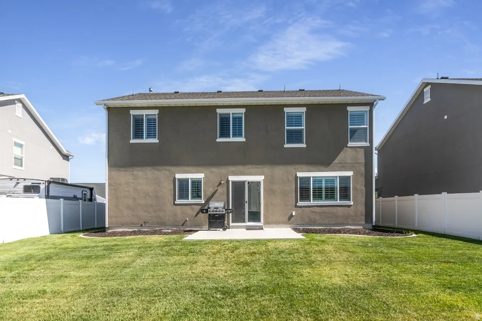 Expansive backyard with a manicured lawn, concrete patio, and mature landscaping beds