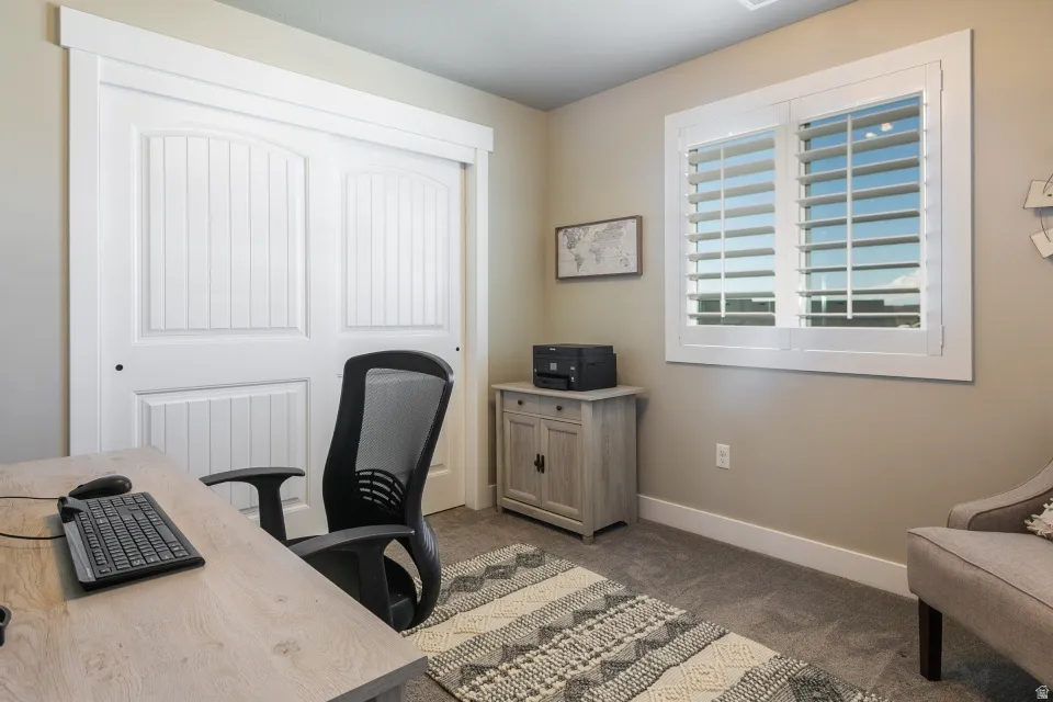 Carpeted room featuring a window with white plantation shutters, white trim, and a built-in closet with white panel doors