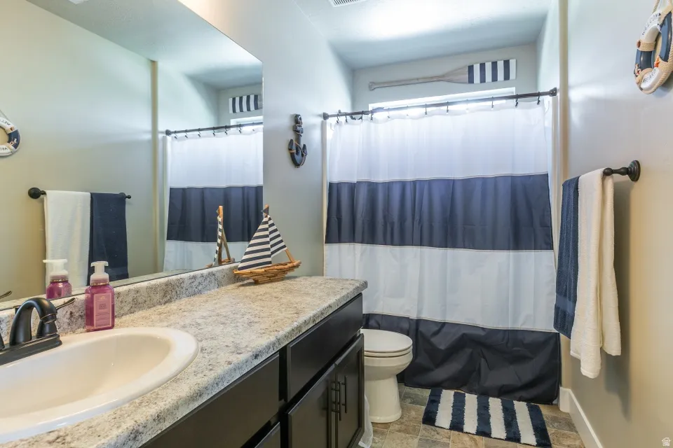 Vanity with integrated sink, speckled countertop, dark wood-finish cabinetry, and framed mirror