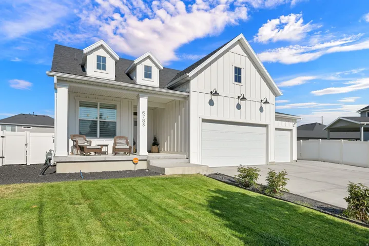 White board and batten siding, multiple dormer windows, covered front porch, attached multi-car garage, and a concrete driveway