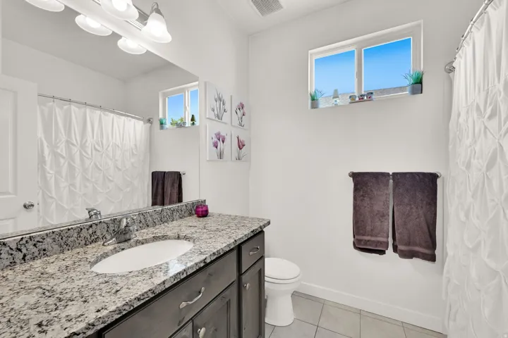Spa-inspired bathroom featuring a granite-topped double vanity with dark cabinetry, ceramic tile flooring, and polished chrome hardware