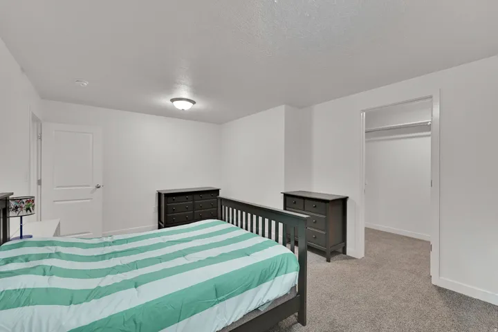 Carpeted flooring, white walls, overhead ceiling light fixture, white door, and an open closet with shelving and hanging rods