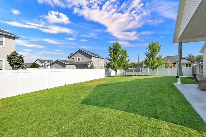 Expansive backyard featuring a manicured lawn, white privacy fencing, and mature trees
