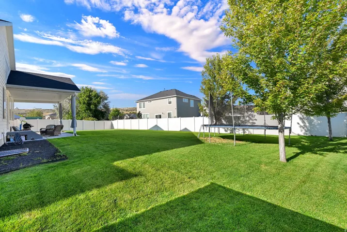 Expansive grassy backyard featuring a covered patio, a full privacy fence, and mature trees