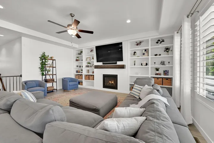 Built-in shelving, fireplace, wood mantel, ceiling fan, and plantation shutters