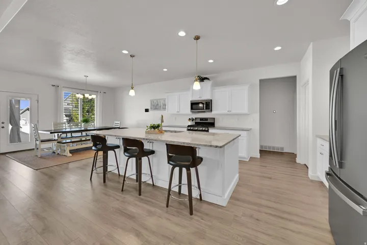 Open-concept kitchen and dining space featuring wood-finish flooring, white cabinetry, a kitchen island with stone countertop, and recessed lighting