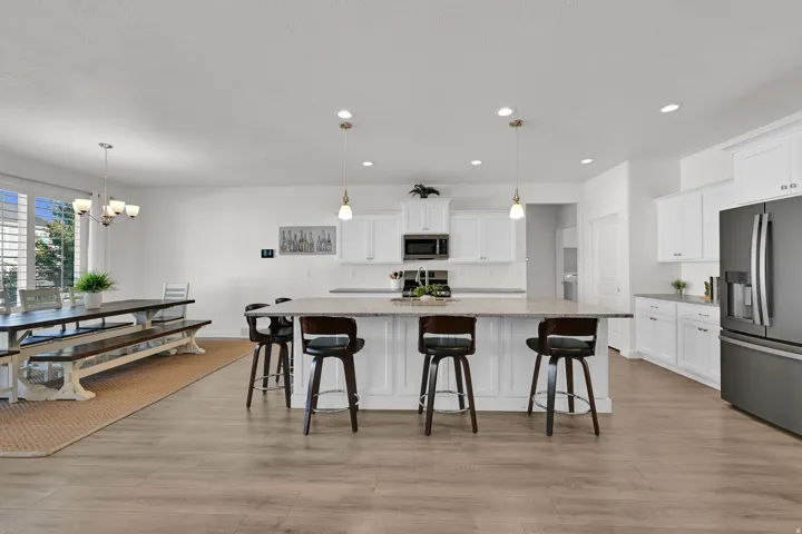 Open-concept living space with wood-finish flooring, white cabinetry, a kitchen island with seating, a full suite of stainless-steel appliances, and recessed lighting