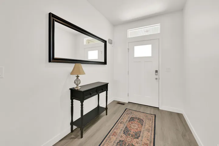 Entryway featuring a solid white door with glass paneling, transom window, and wood-finish flooring