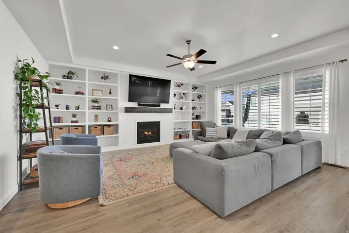 Tray ceiling with recessed lighting, built-in shelving, a modern fireplace, wood-finish flooring, and multiple windows with plantation shutters