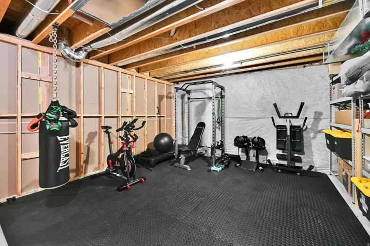 Exposed ceiling joists with visible ductwork, unfinished wall framing, and durable black rubber flooring