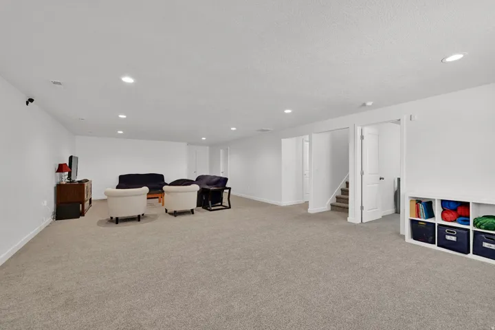Expansive carpeted room with recessed lighting, an integrated storage unit, and access to a staircase