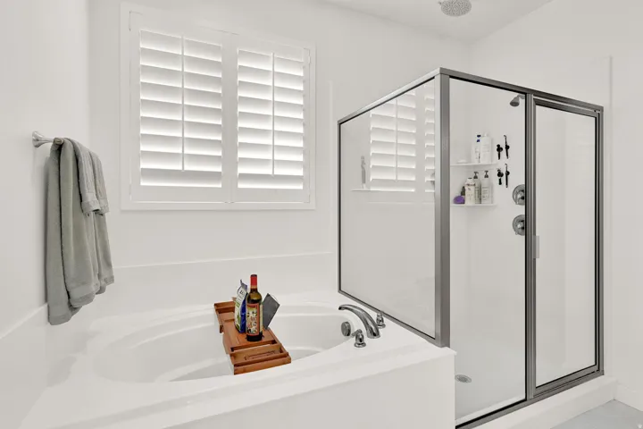 Soaking tub with deck-mounted faucet, plantation shutters, and a glass-enclosed shower with rain head