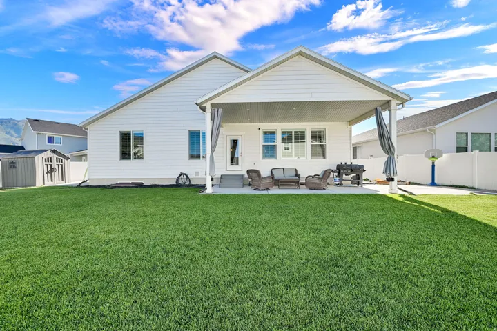 Expansive backyard featuring a large green lawn, covered patio, white siding, and a storage shed