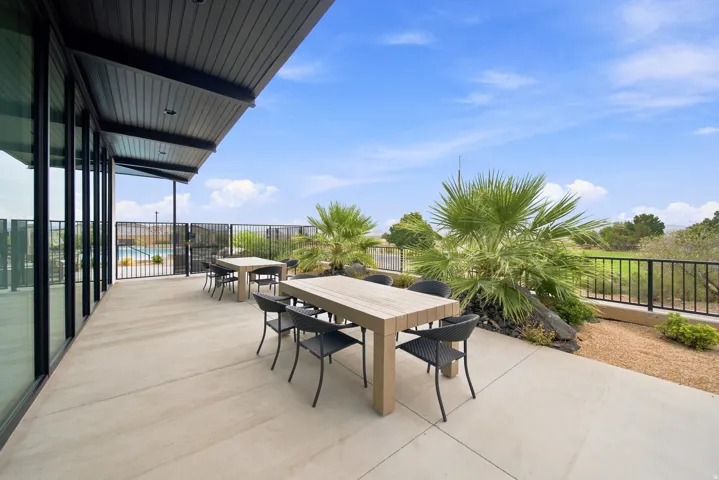 Expansive concrete patio featuring a black slatted overhang, full-height glass panels, black metal railing, and desert landscaping