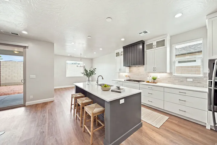 Modern kitchen featuring white cabinetry, a center island with seating, wood-finish flooring, a stainless steel gas range, and a sliding glass door leading to the backyard