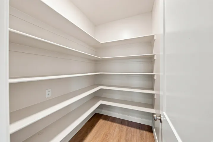 Walk-in pantry with extensive built-in shelving, wood-finish flooring, and a neutral color palette