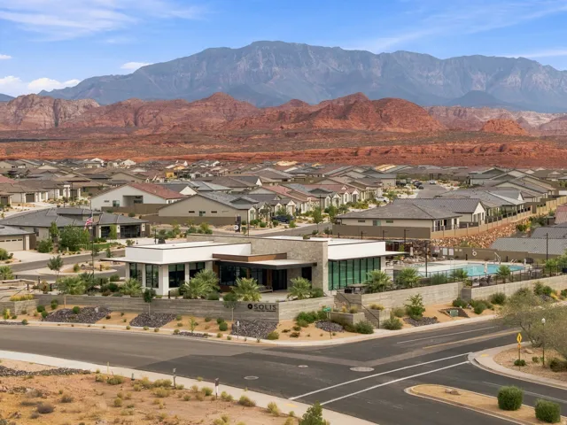 Modern residential community with a clubhouse, swimming pool, and desert landscaping, set against a backdrop of prominent mountains