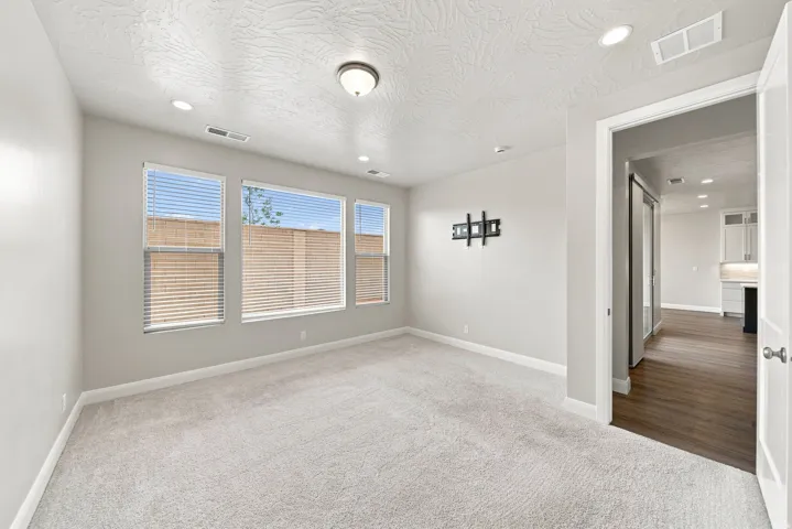Plush carpeting, recessed lighting, and a ceiling-mounted light fixture illuminate this room with multiple windows