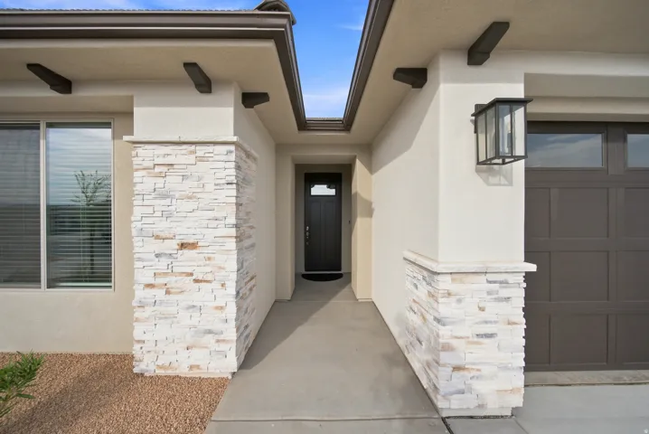 Stucco exterior with stacked stone accents, dark wood-look garage door, and a covered entry