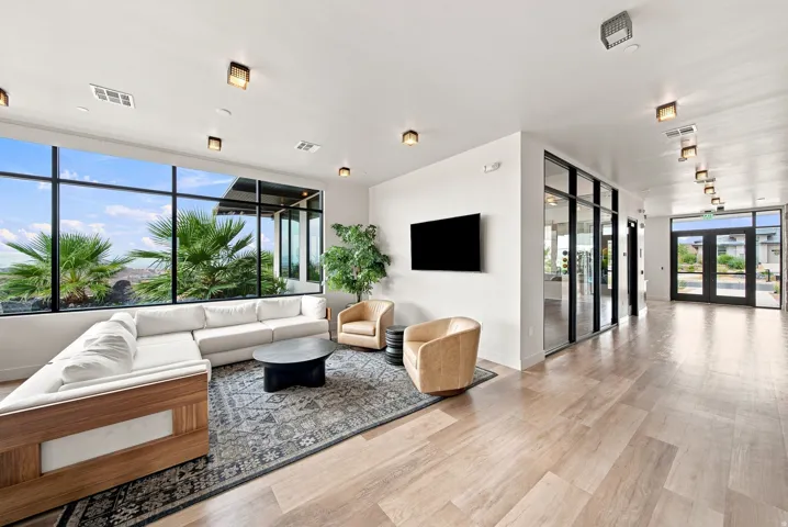 Spacious lounge area featuring large format windows, wood-finish flooring, recessed lighting, and a wall-mounted display