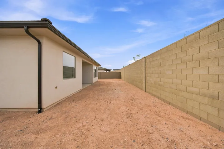 Stucco exterior with multiple windows, concrete block perimeter wall, and a covered patio area