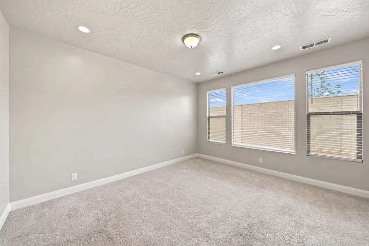 Recessed lighting with a central flush mount fixture, light-toned carpeting, multiple windows with blinds, and neutral wall paint