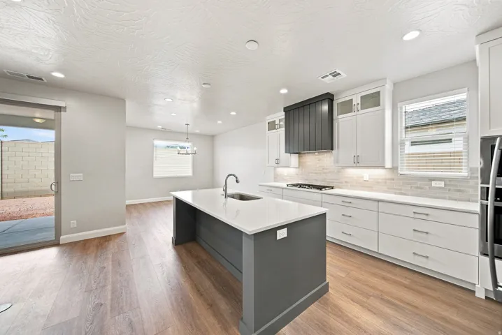Modern kitchen featuring a large center island with sink, white shaker cabinetry, stainless steel appliances, and wood-finish flooring