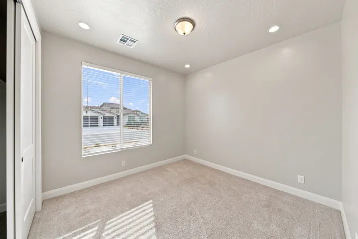 Recessed ceiling lighting, flush mount ceiling fixture, large window with blinds, light-toned carpet flooring, and a sliding closet door