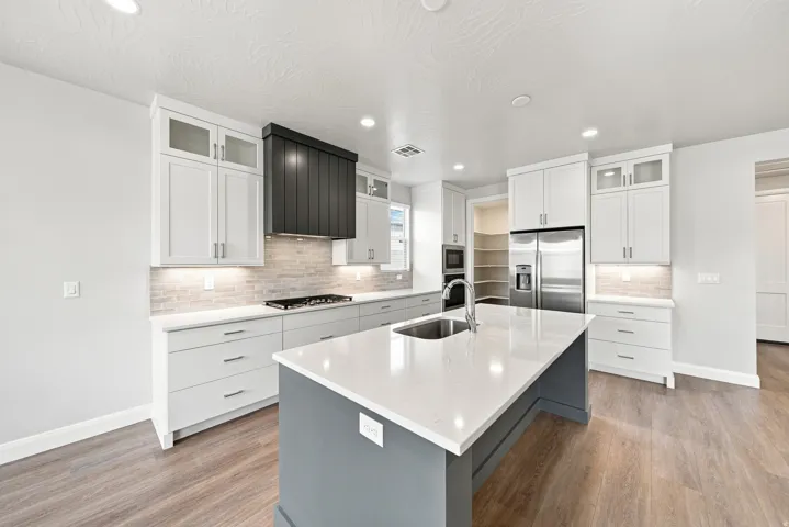 Kitchen featuring white shaker cabinetry, stainless steel appliances, a center island with a sink, and wood-finish flooring