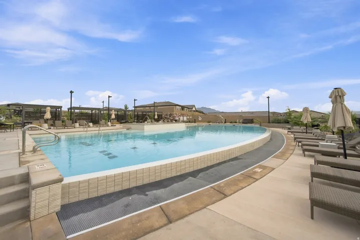 Expansive swimming pool with integrated steps, surrounded by a concrete deck and multiple poolside lounge chairs