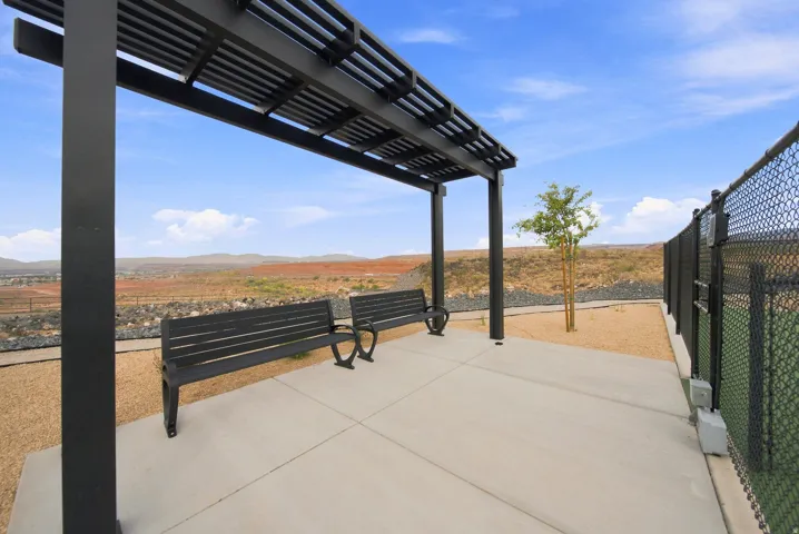 Outdoor concrete patio featuring a black metal pergola, two black benches, and a chain-link fence